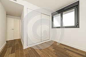 Empty room with a built-in wardrobe with white wooden sliding doors, black anodized aluminum windows and dark stoneware floors