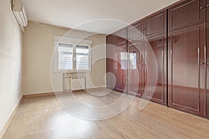 Empty room with built-in wooden wardrobe covering a bright reddish wall