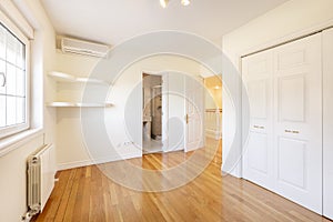 Empty room with fitted wardrobes with white lacquered doors, built-in shelves in one corner, en-suite marble bathroom and pine