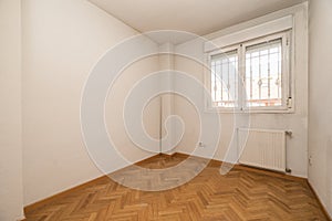 Empty room with herringbone oak parquet flooring, white aluminum radiator under matching aluminum window