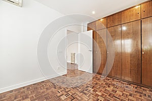 An empty room with a large built-in wardrobe with wooden doors covering one wall