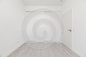 An empty room in a loft-type home with a built-in wardrobe covering the entire wall with white wooden sliding doors