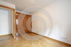 Empty room with old-style glossy wooden wardrobe and French oak parquet floor laid in a herringbone pattern