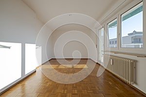 Empty room with parquet flooring, under the window there is a large radiator. From the door you can go out onto the small balcony