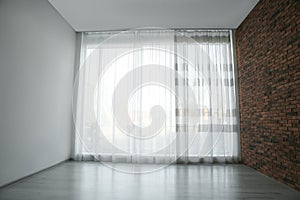 Empty room with red brick wall, large window and wooden floor