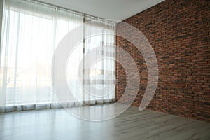 Empty room with red brick wall, large window and wooden floor