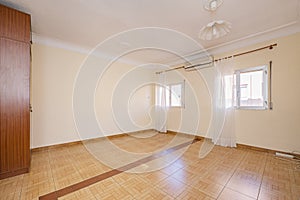 Empty room with stoneware floor, air conditioner between two aluminum windows with white curtains