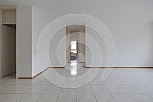 Empty room with tiles and white walls. The door is open to the bathroom