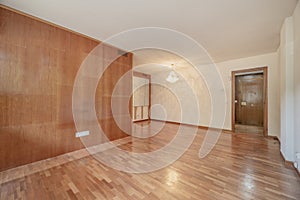 Empty room with a wall covered with a wooden varnish mural in a color that matches the parquet floors