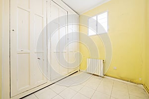 An empty room with walls covered by a large built-in wardrobe with vintage-style white wood doors and yellow painted walls