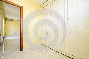 An empty room with walls covered by a large built-in wardrobe with vintage-style white wooden doors and yellow painted walls, a