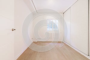 An empty room with walls covered in white cabinets with Venetian style sliding doors and French style aluminum windows