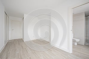 Empty room with white fitted wardrobes, white walls and wood-like ceramic