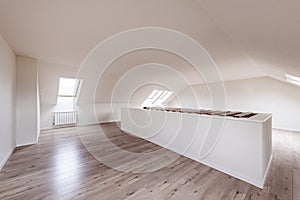 Empty room with white painted walls and chestnut parquet flooring and sloping ceilings with skylights