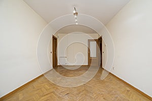 Empty room with white painted walls, herringbone oak parquet flooring,