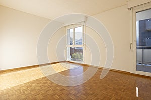 Empty room with white walls and parquet. There is a window overlooking nature