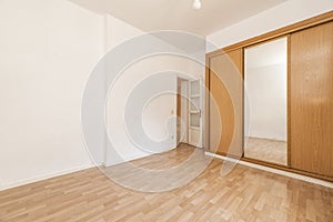 Empty room with wooden built-in wardrobe with cherry-colored sliding doors and white wooden access door and matching laminated