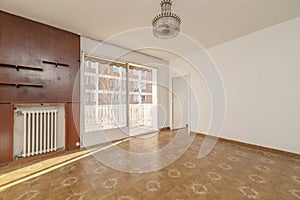 Empty room with a wooden covered wall, a cast iron radiator and an exit to a terrace with large sliding glass doors