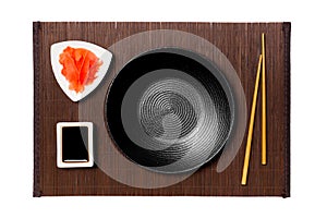 Empty round black plate with chopsticks for sushi, ginger and soy sauce on dark bamboo mat background. Top view with copy space