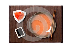 Empty round brown plate with chopsticks for sushi, ginger and soy sauce on dark bamboo mat background. Top view with copy space