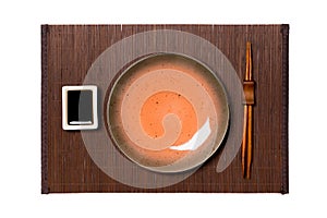 Empty round brown plate with chopsticks for sushi and soy sauce on dark bamboo mat background. Top view with copy space for you