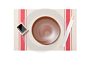 Empty round brown plate with chopsticks for sushi and soy sauce on sushi mat background. Top view with copy space for you design