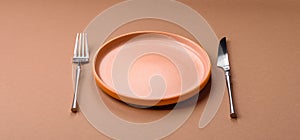 An empty round ceramic plate, knife, and fork as a dining table setting. An empty plate