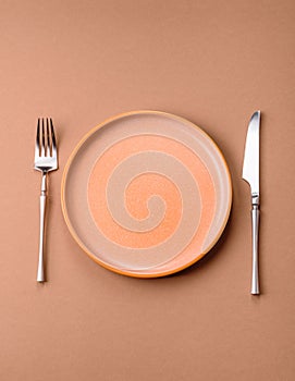 An empty round ceramic plate, knife, and fork as a dining table setting. An empty plate