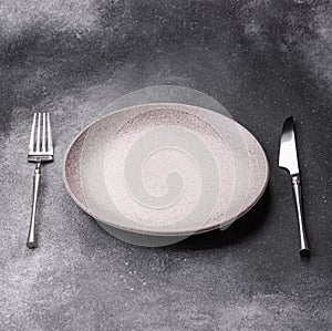 An empty round ceramic plate, knife, and fork as a dining table setting. An empty plate