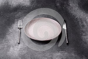 An empty round ceramic plate, knife, and fork as a dining table setting. An empty plate