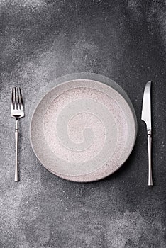 An empty round ceramic plate, knife, and fork as a dining table setting. An empty plate