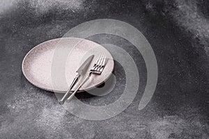 An empty round ceramic plate, knife, and fork as a dining table setting. An empty plate