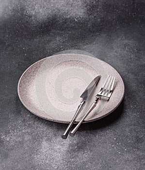 An empty round ceramic plate, knife, and fork as a dining table setting. An empty plate