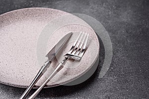 An empty round ceramic plate, knife, and fork as a dining table setting. An empty plate