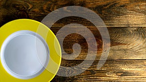 Empty round ceramic plate with yellow edge on rough wooden background or table. Copy space for text. Top down. Flat lay. 16x9