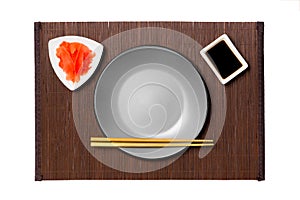 Empty round gray plate with chopsticks for sushi, ginger and soy sauce on dark bamboo mat background. Top view with copy space for