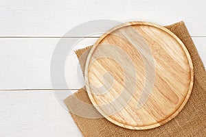 Empty round wooden plate with rustic brown burlap cloth on white wooden table.