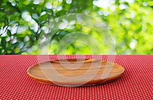 Empty round wooden tray on red polka dot tablecloth over blur tr