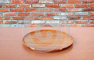 Empty round wooden tray on table over brick wall background.