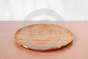 Empty round wooden tray on table over white wall.
