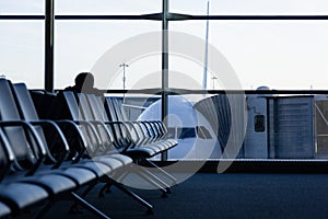 Empty row of seats in waiting area at airport with airplane on background