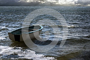 Empty rowboat floats lonely on the sea waves to the clouds at th