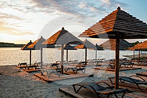 Empty rows resting places on evening sandy beach with brown wooden loungers and umbrellas
