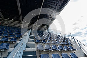 Empty Rows of stadium grandstand seats or stadium seats with sunray on roof and cloud sky, plastic blue and white seats on grand s