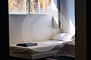 Empty rustic room of cheap hotel apartments with bed white sheet and morning sun light ray through window