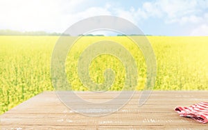 Empty rustic wooden table with blue tablecloth over rapeseed yellow field on sunny summer day background. Harvest mock up