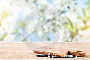 Empty rustic wooden table with blue tablecloth and wooden board over rapeseed blooming summer garden on sunny day