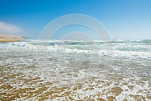 Empty sand beach, ocean waves, and clear blue sky on background