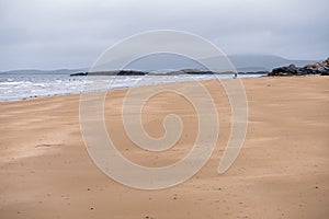 Empty sandy beach at low tide and blue water of Atlantic ocean. West coast of Ireland. Cloudy low sky. Irish nature landscape