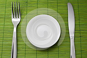 Empty saucer, fork and knife placed on colored mat background